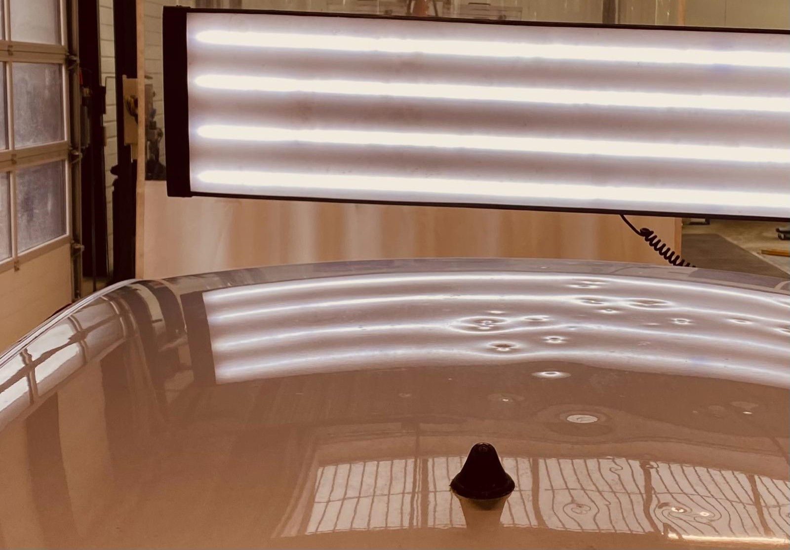 Pavillon grêlé sous une lampe de débosselage : chaque impact déforme les bandes lumineuses